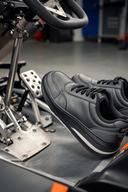 Kartingschoenen met dunne zool naast pedalen van een kart in een werkplaats